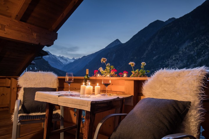 Ein Tisch, der mit zwei Stühlen auf einem Balkon und einer brennenden Kerze dekoriert ist, schafft eine einladende Atmosphäre.