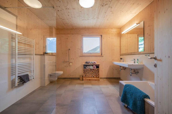 Wood-clad bathroom with glass shower, bathtub, WC, two washbasins and window