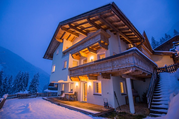 The Alpenkönigin house in a snowy setting, with a wooden terrace that invites you to relax.