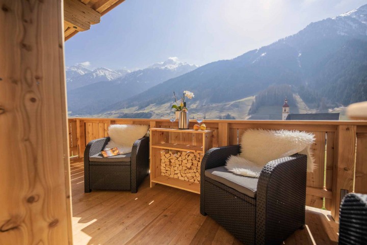 Balkon mit geflochtenen Stühlen und Aussicht auf beeindruckende Berglandschaft.