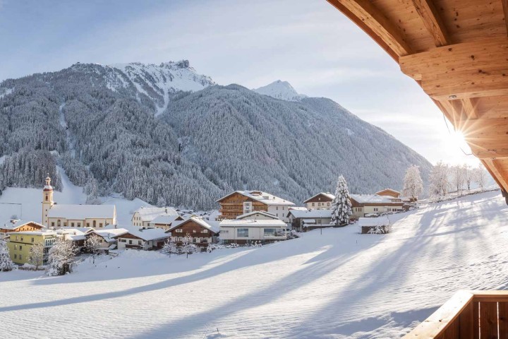 Blick vom Balkon auf ein idyllisches Dorf in den Bergen, umgeben von Schnee und majestätischen Gipfeln.