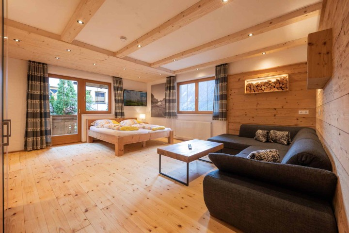Ferienwohnung mit warmen Holzwänden und einem komfortablen Bett im Raum sowie einer Couch und Zugang zum Balkon