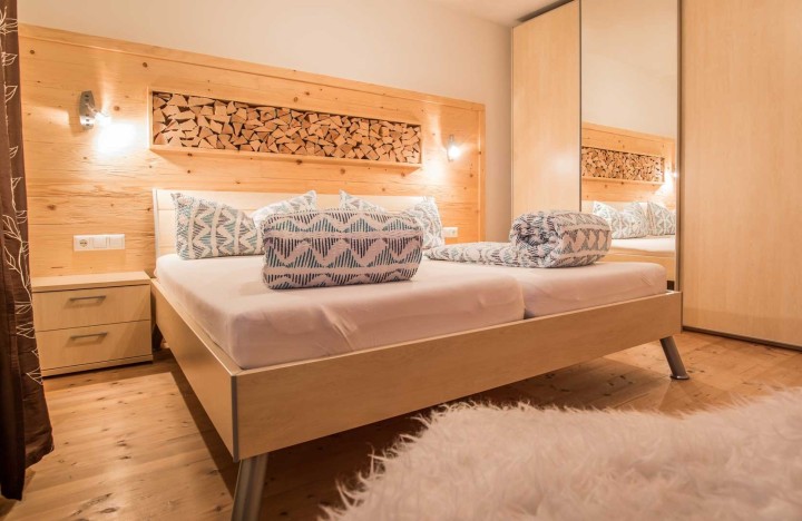 Schlafzimmeransicht mit einem Bett und einer rustikalen Holzwand, die Wärme und Komfort vermittelt.