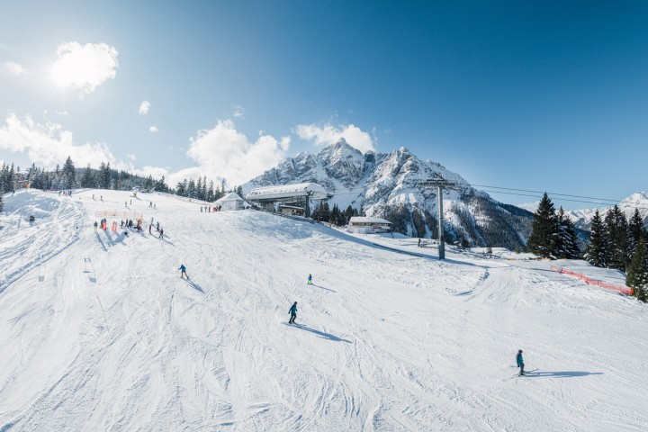 Piste with skiers and lifts in sunshine and perfect snow conditions