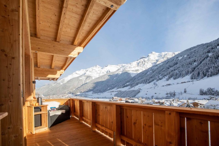 Ausblick vom Balkon auf das schneebedeckte Stubaital mit Häusern und Bergen im Hintergrund bei strahlendem Sonnenschein